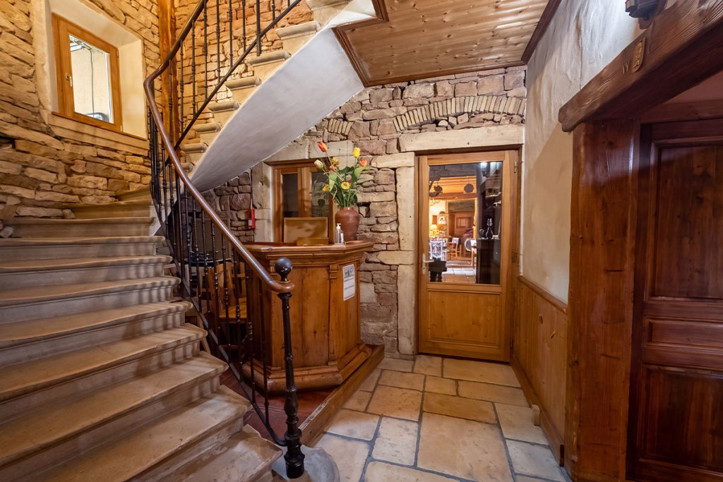 Hall d'entrée de l'hôtel à Tournus, avec sa réception en bois et son escalier en pierre menant aux chambres